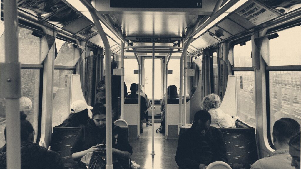 Commuters seated in a London DLR carriage, framed by teal grab rails and lit by the end door.