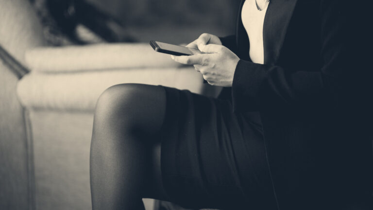Person in work uniform typing on a phone while seated indoors, face out of frame, warm muted tones
