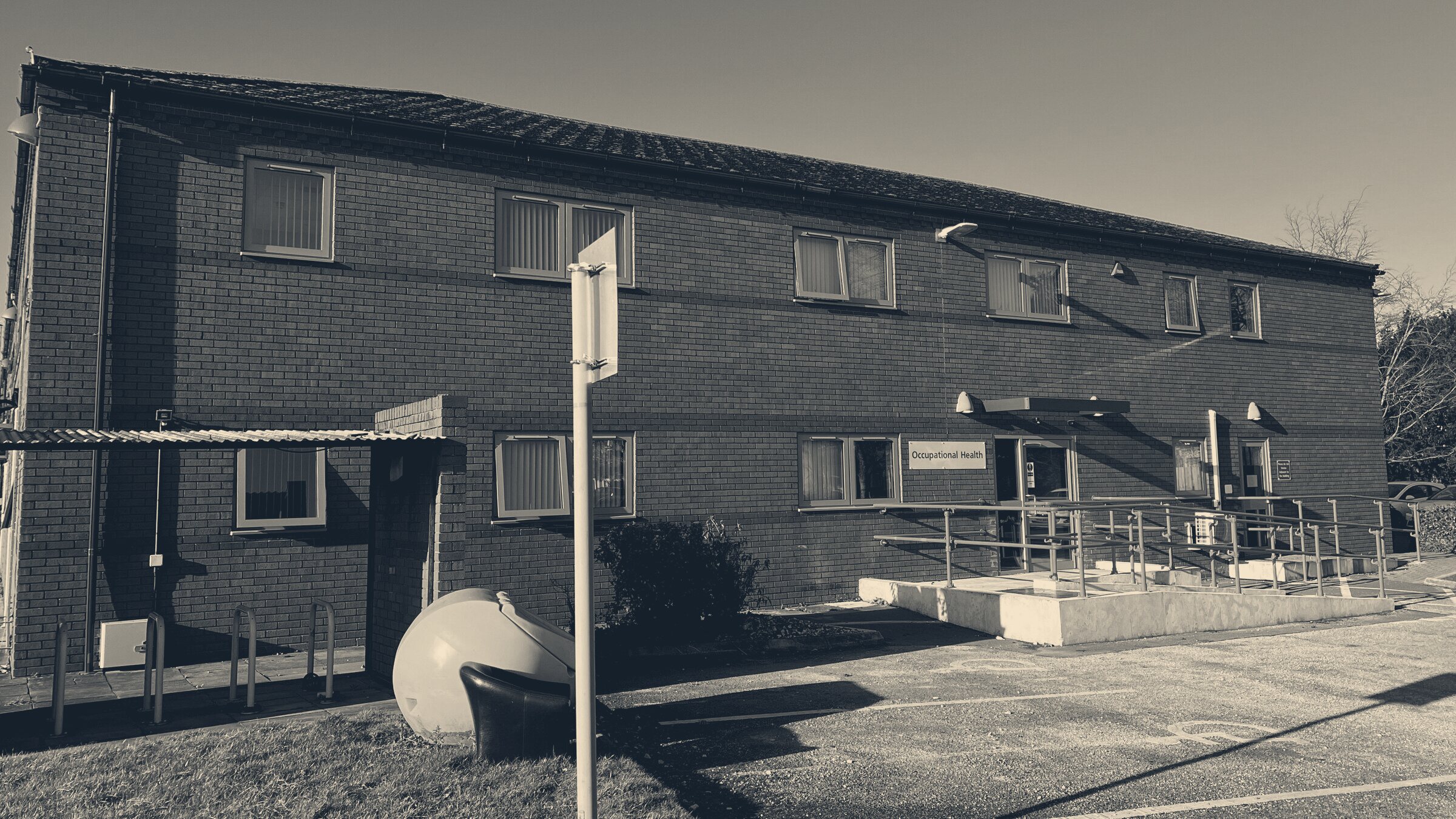 Brick occupational health department at a UK hospital, blue ramp rails leading to the entrance in winter sun