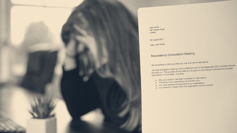 A dismissal letter titled 'Redundancy Consultation Meeting' in sharp focus beside a blurred worker with head in hand.