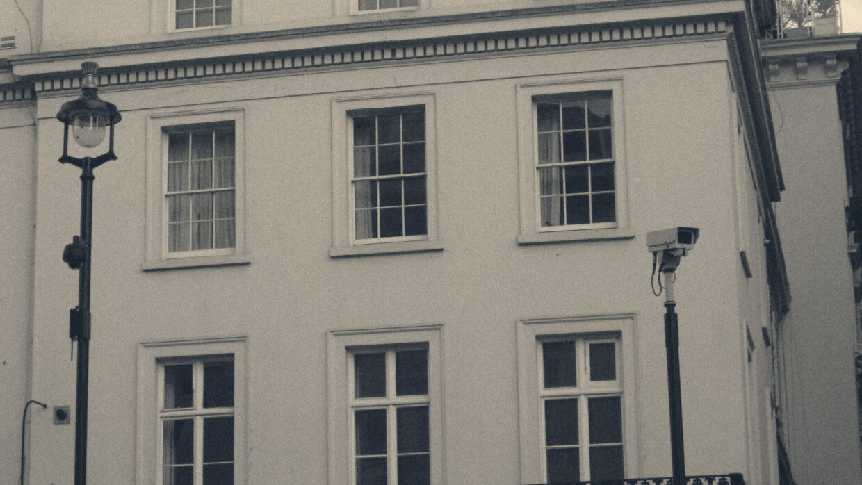 A CCTV camera on a pole trained on the sash windows of a white Georgian terrace in London