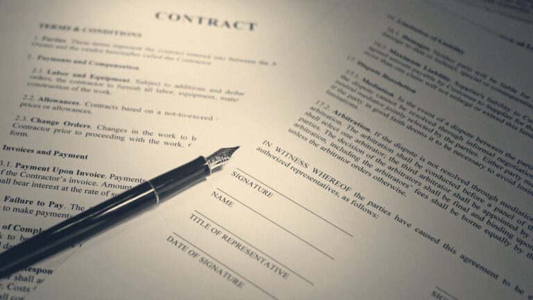 A fountain pen rests beside the signature lines of a printed contract, clause text soft in the light