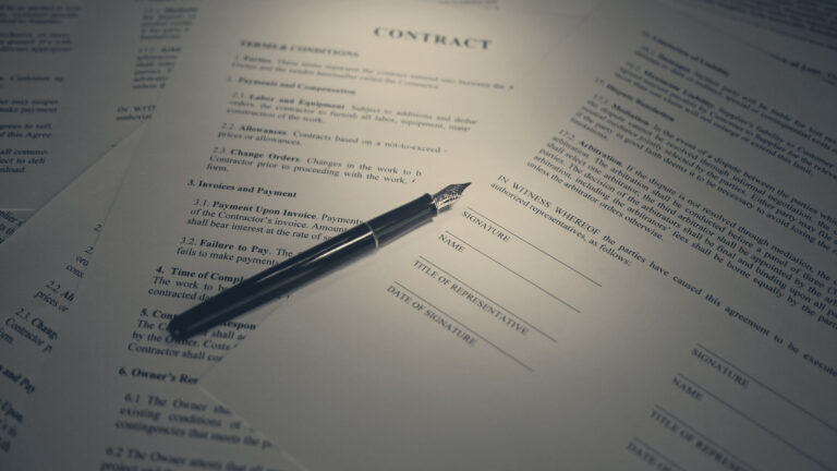 A fountain pen rests on the signature block of a printed contract, surrounded by more contract pages.