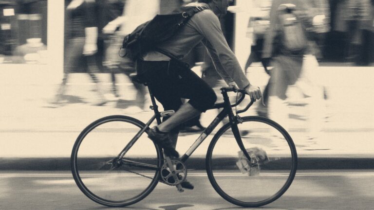 A courier cycles along Oxford Street, London, shot in profile against motion-blurred pedestrians and shopfronts.
