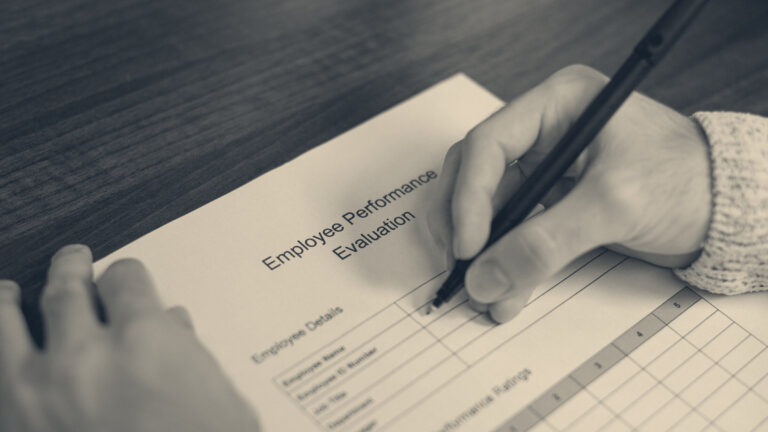 A worker holding a pen above an employee performance evaluation form on a wooden desk
