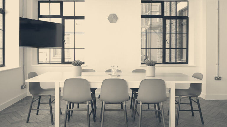Conference table and grey chairs arranged for a hearing, with note pencils, wall clock, and Crittall windows in London.