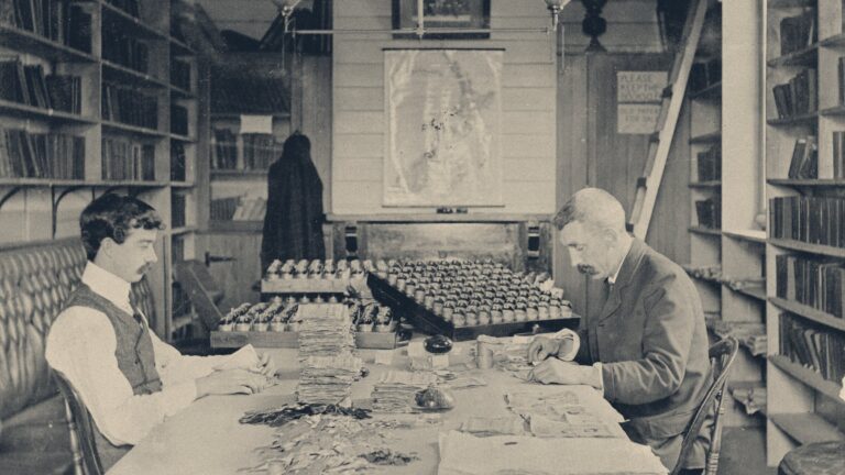 Railway clerks counting coins and banknotes into pay packets at a ledger-lined table
