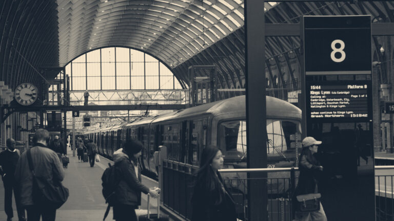 Commuters on a King's Cross platform beneath a departures board and platform clock