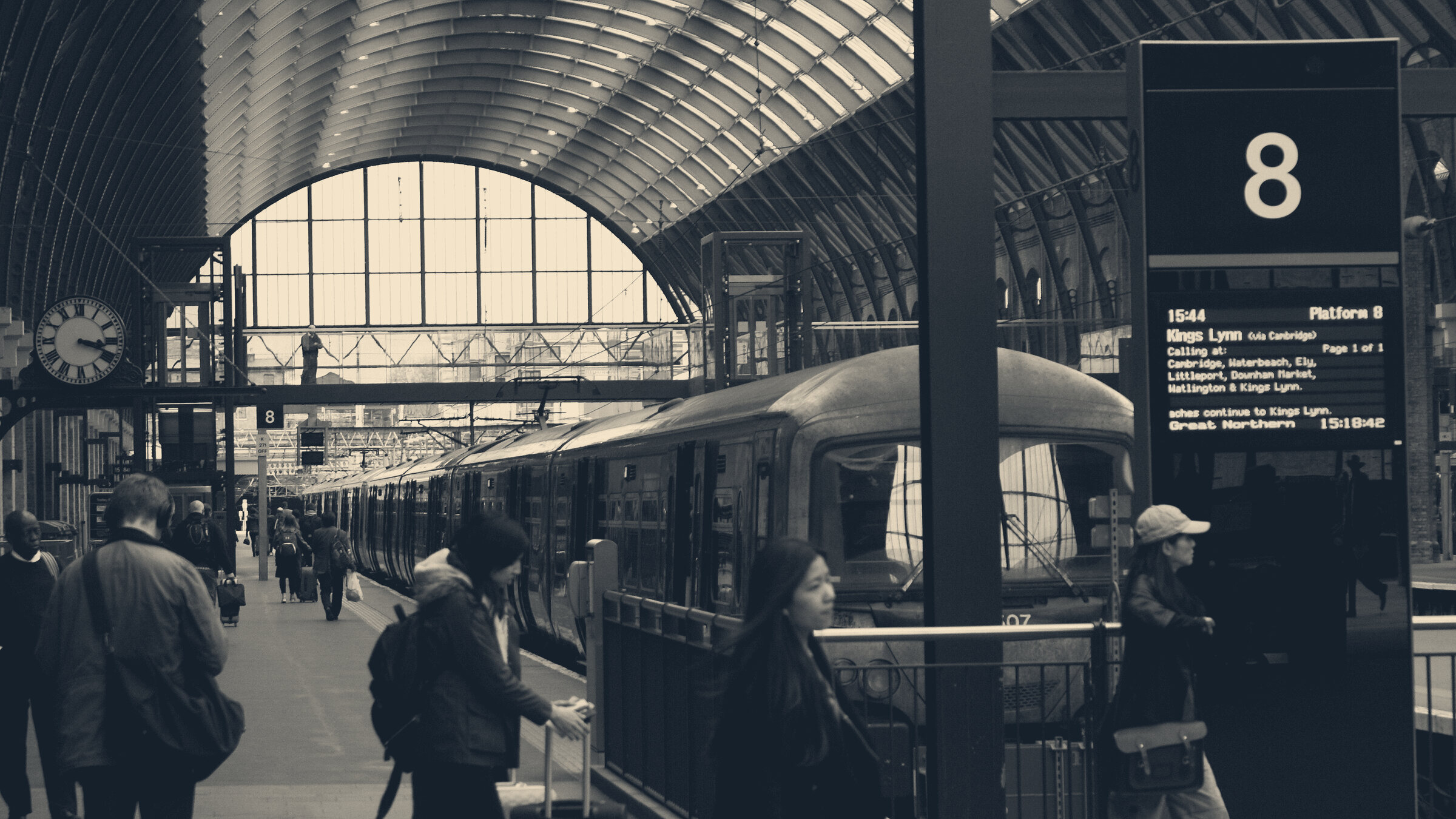 Commuters on Platform 8 at London King's Cross, beneath the arched roof beside a departures board.