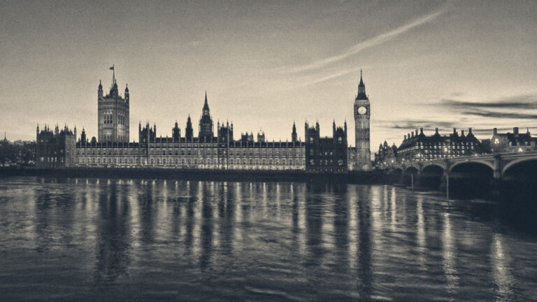 Palace of Westminster and the Elizabeth Tower clock face lit up at dusk, reflected in the River Thames.