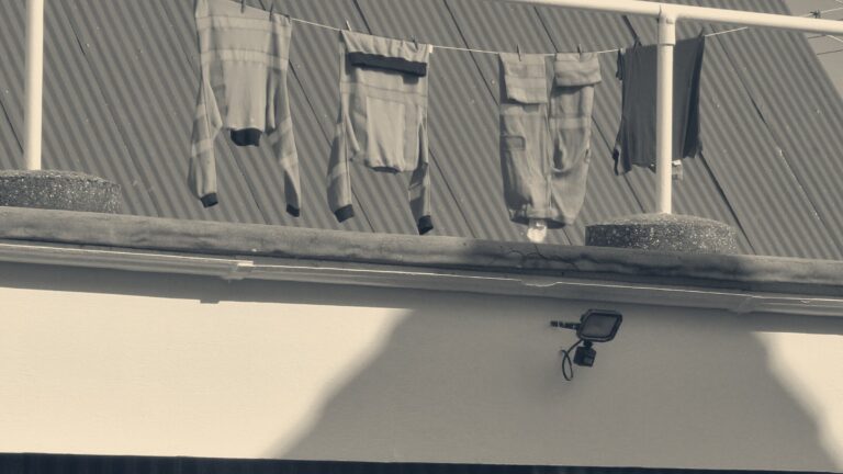 Orange high-visibility jackets and overalls pegged on a washing line in front of a green corrugated shed roof.