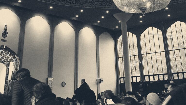 Worshippers at Friday prayer inside London Central Mosque, beneath arched windows and a chandelier