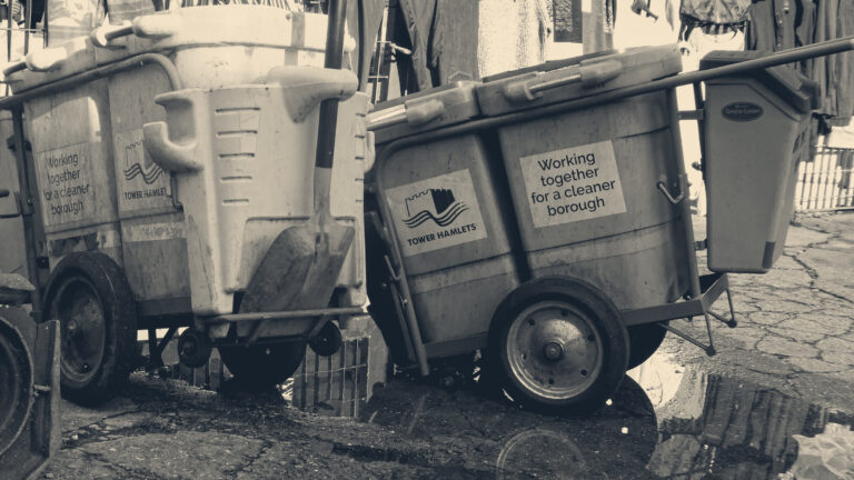 Street cleaner's carts and an orange shovel beside a puddle at Brick Lane market, east London