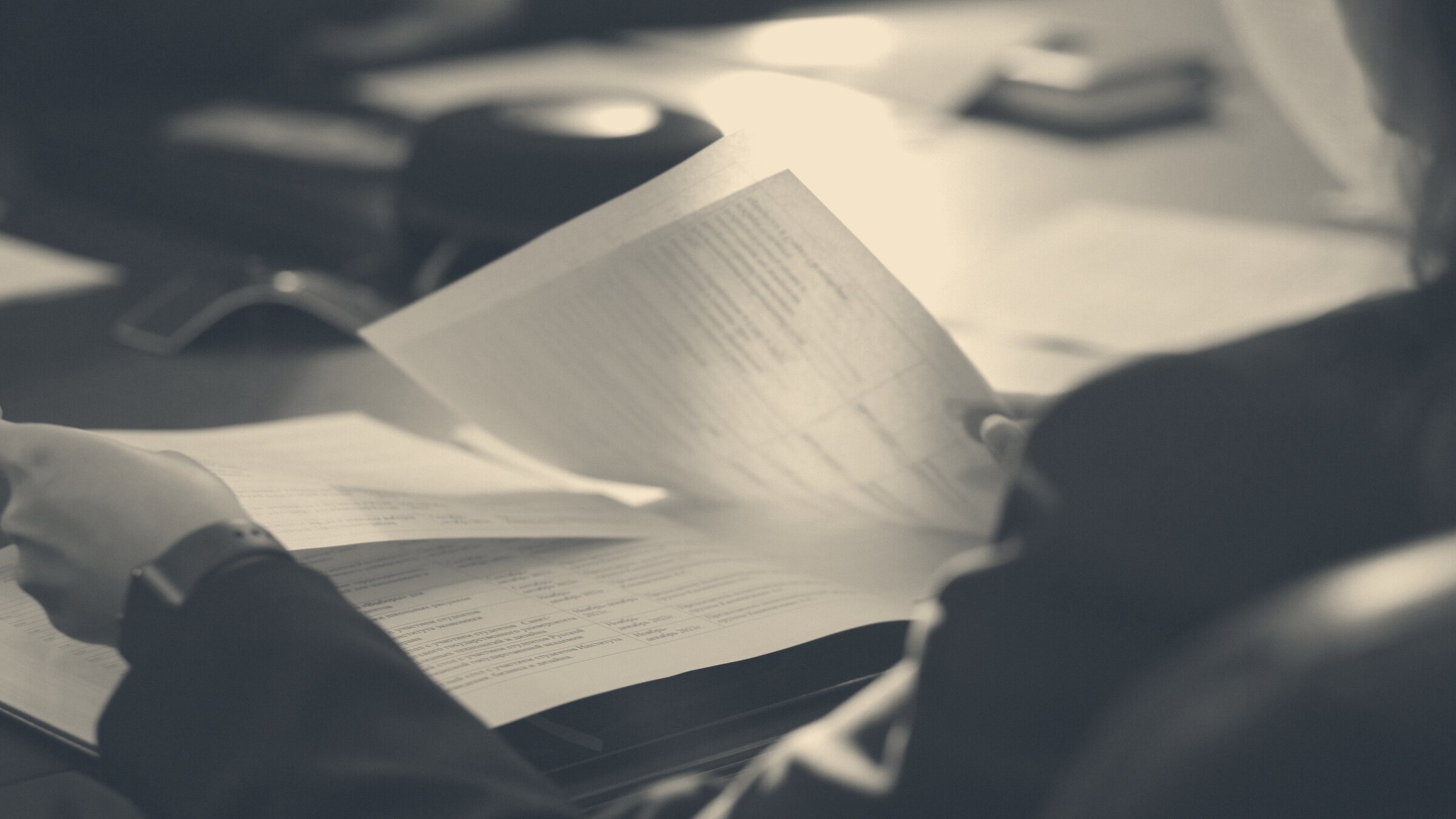 A professional in a dark blazer reviews pages of a printed agreement across a meeting room conference table.