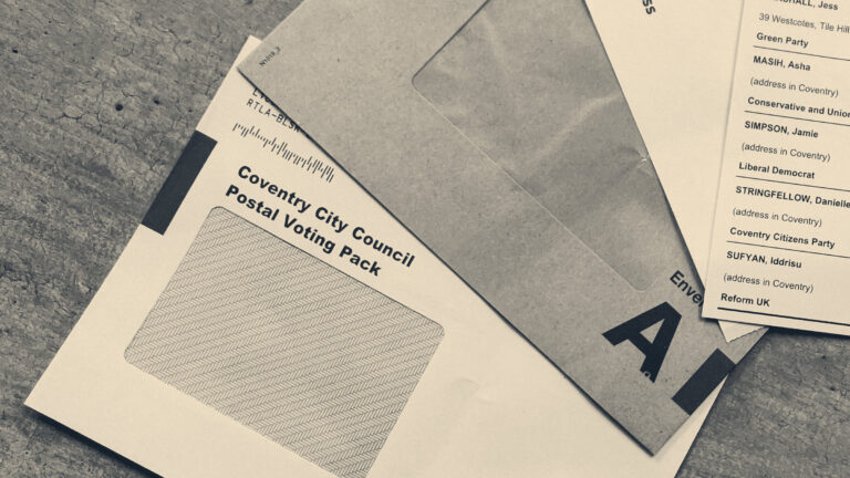 A UK council postal voting pack, ballot envelope and ballot papers spread on a grey desk.