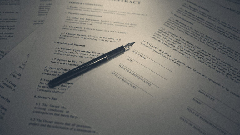 Fountain pen resting on a contract's signature block beside a printed arbitration clause, lit from the side.