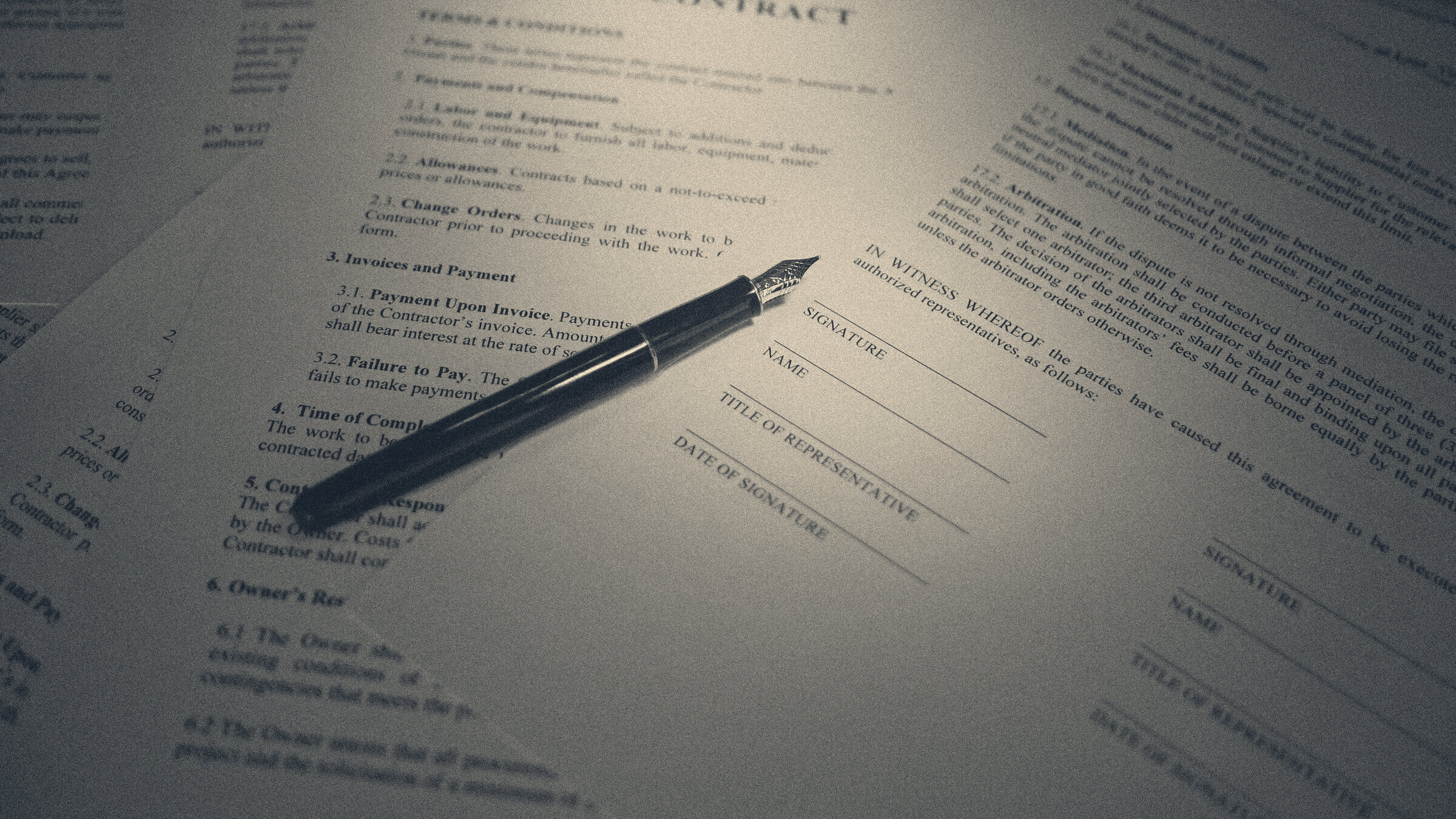 Fountain pen resting on a contract's signature block beside a printed arbitration clause, lit from the side.