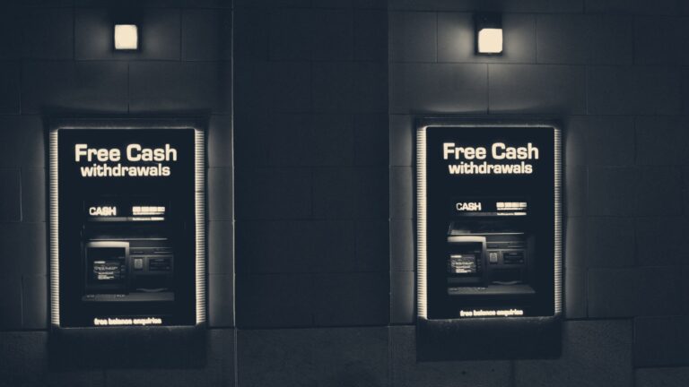 Two blue-lit cash machines recessed in a stone wall at night, sign reading free cash withdrawals