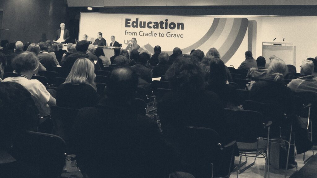 Delegates seen from behind facing a stage and speaker at a union congress event inside TUC Congress Hall, London.