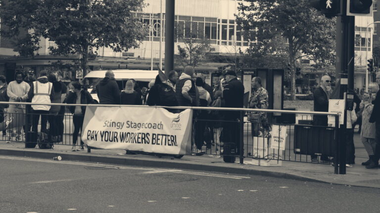 Bus drivers on a picket line in Hull hold a Unite banner reading 'Stingy Stagecoach pay your workers better'.