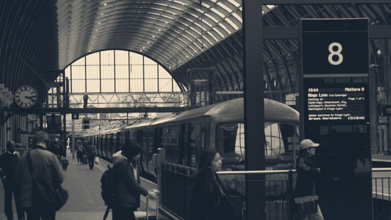 Commuters with luggage walk along platform 8 at London King's Cross station beneath the arched train shed roof.