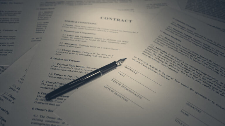 A fountain pen rests beside the signature line on a contract headed CONTRACT, under a spotlight.
