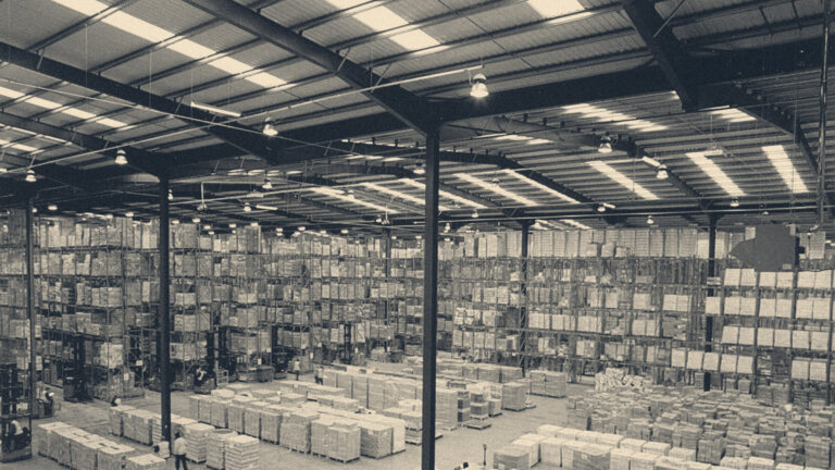 Vast logistics warehouse in England with high-bay pallet racking, forklift trucks, and shift workers in hi-vis