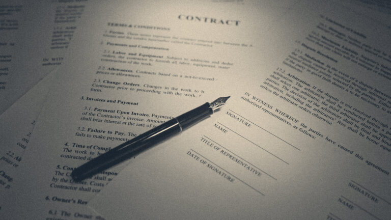 A fountain pen rests across the signature block of a printed contract headed CONTRACT, papers fanned in moody light.