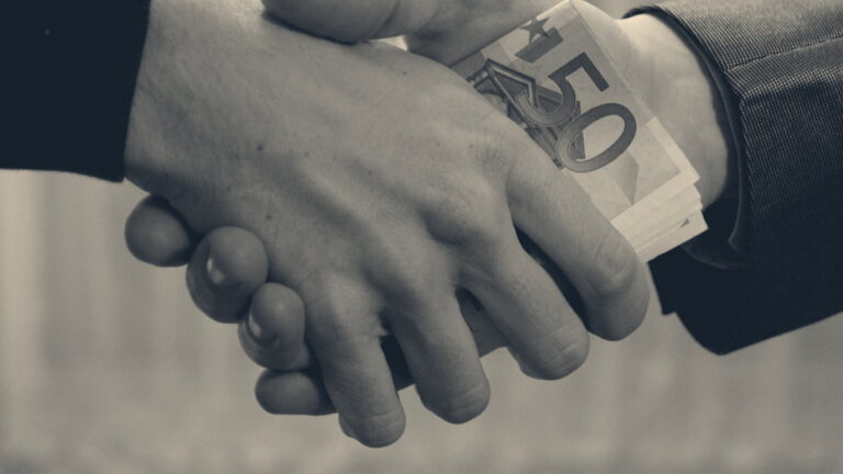 Close-up of a handshake with folded banknotes concealed between the two hands, suit and jumper sleeves