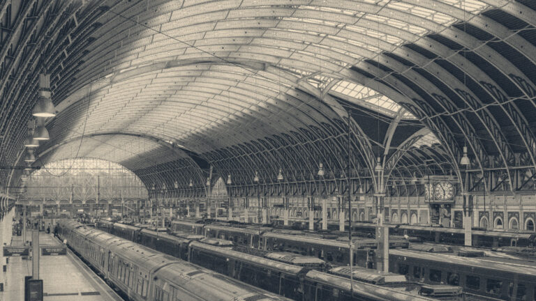 Vaulted iron roof arches, station clock, and passenger trains at London Paddington station.