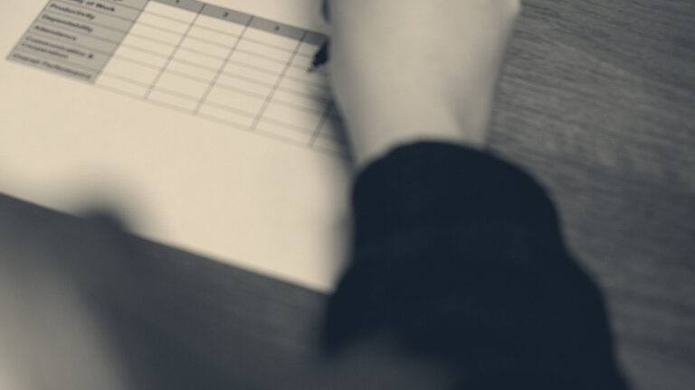 Hand holding a pen over a tick-box monitoring form on a desk, shallow focus