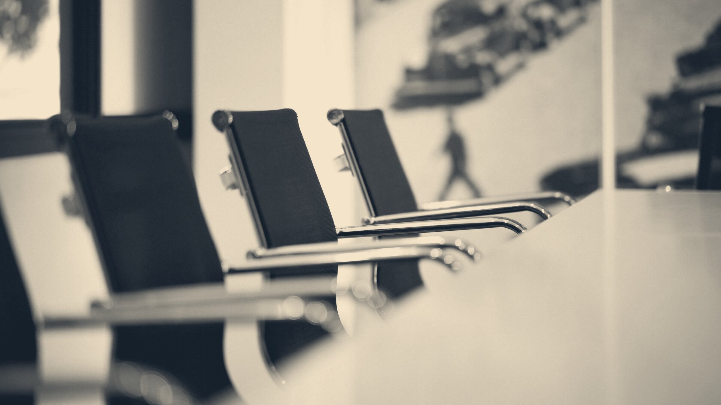 Row of empty black office chairs with chrome armrests along a conference table, shallow depth of field