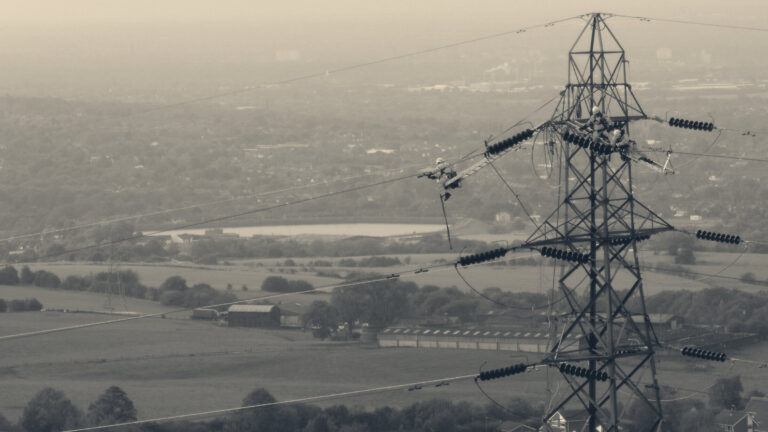 Linesmen in hi-vis gear maintain high-voltage conductors on a National Grid electricity pylon over an English valley.