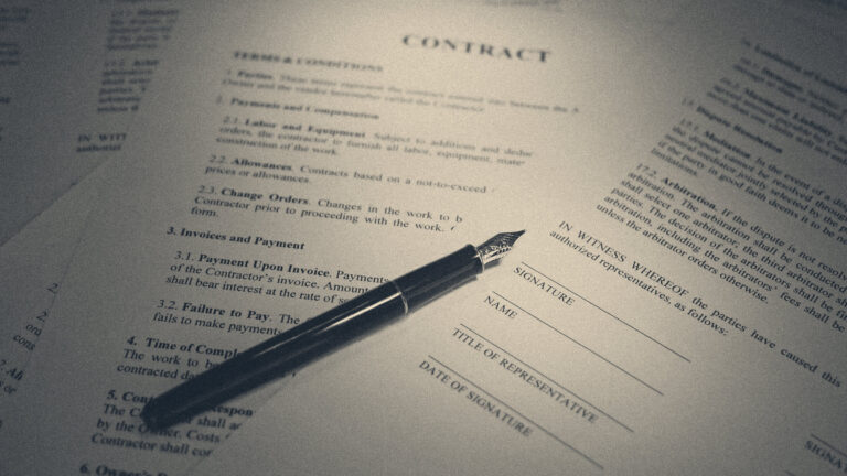 A fountain pen rests on a printed employment contract beside an unsigned signature block under warm light.
