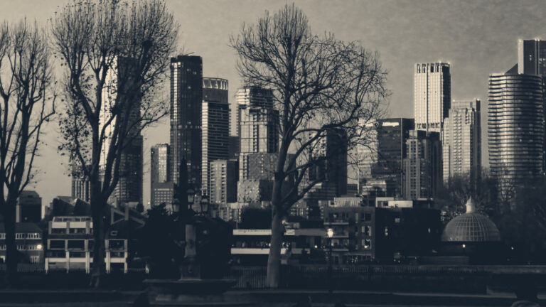 Canary Wharf office towers glowing at dusk, seen through bare winter trees at Greenwich, London