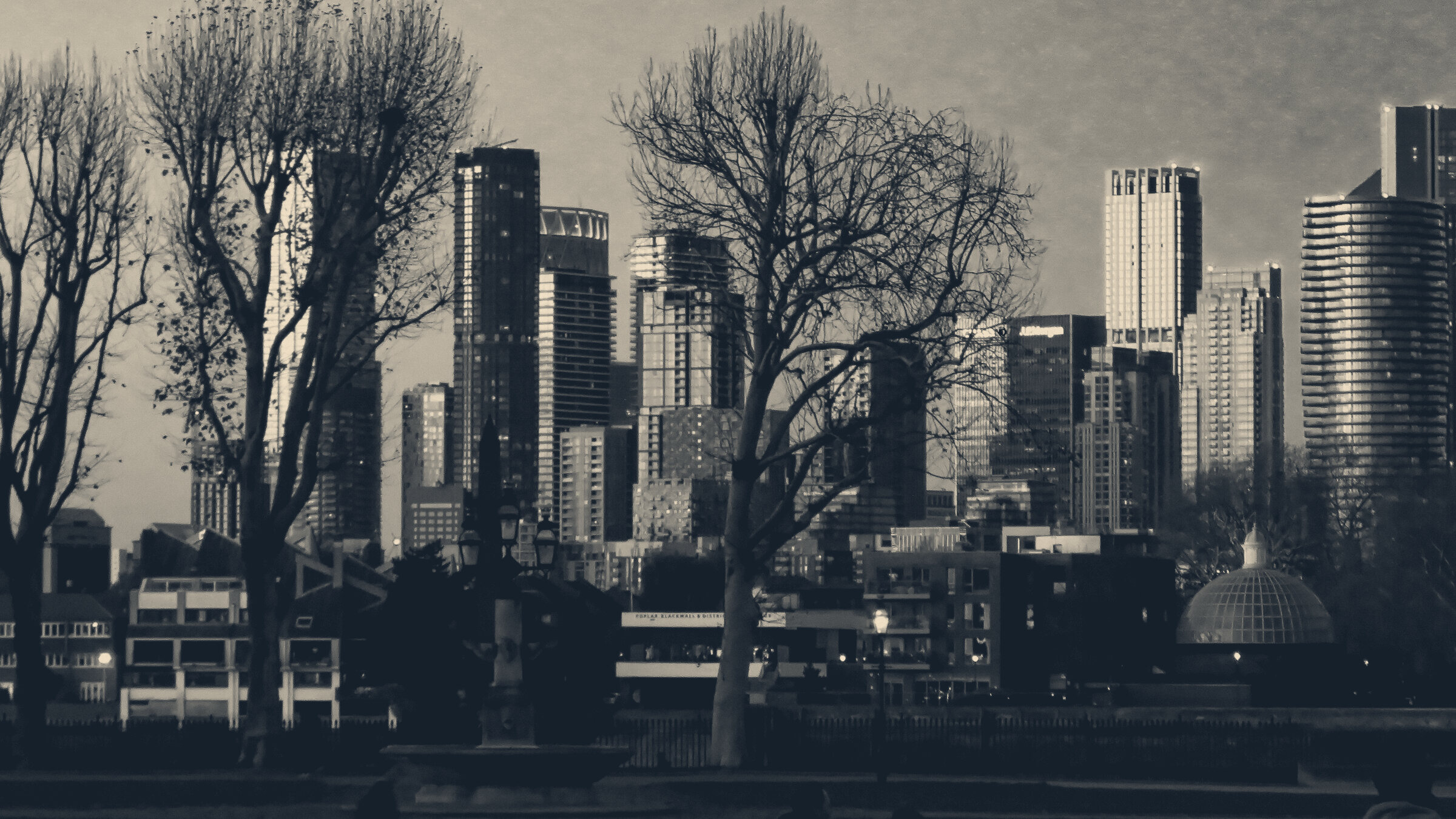 Canary Wharf office towers glowing at dusk, seen through bare winter trees at Greenwich, London