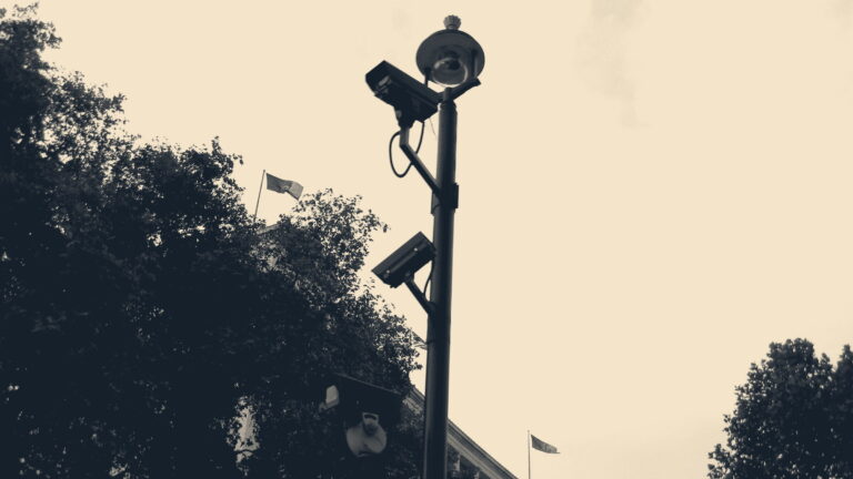 CCTV cameras on a lamp mast silhouetted against a flag-flying government building in London