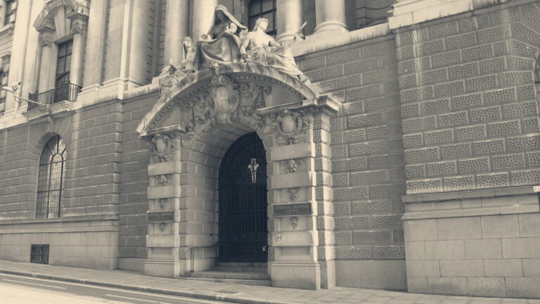 Gated entrance of the Central Criminal Court (Old Bailey), London, beneath carved figures and its street sign