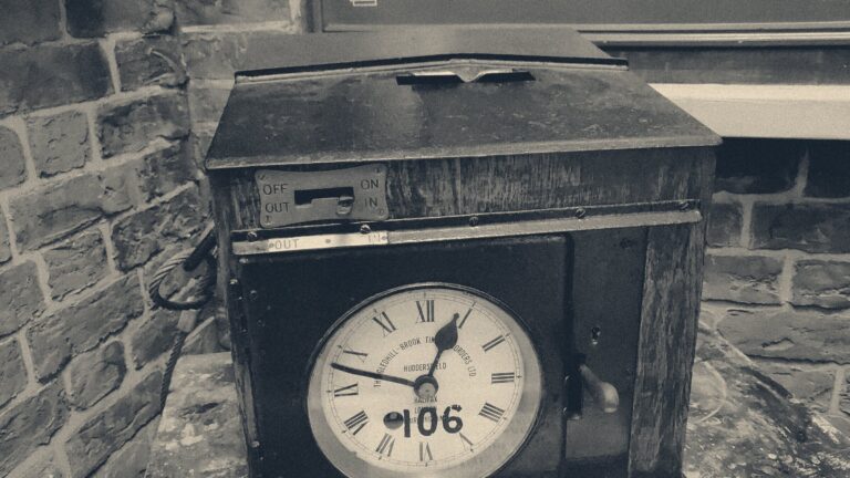 Vintage Gledhill-Brook clocking-in machine from Huddersfield, its time card set to OUT, against a brick wall