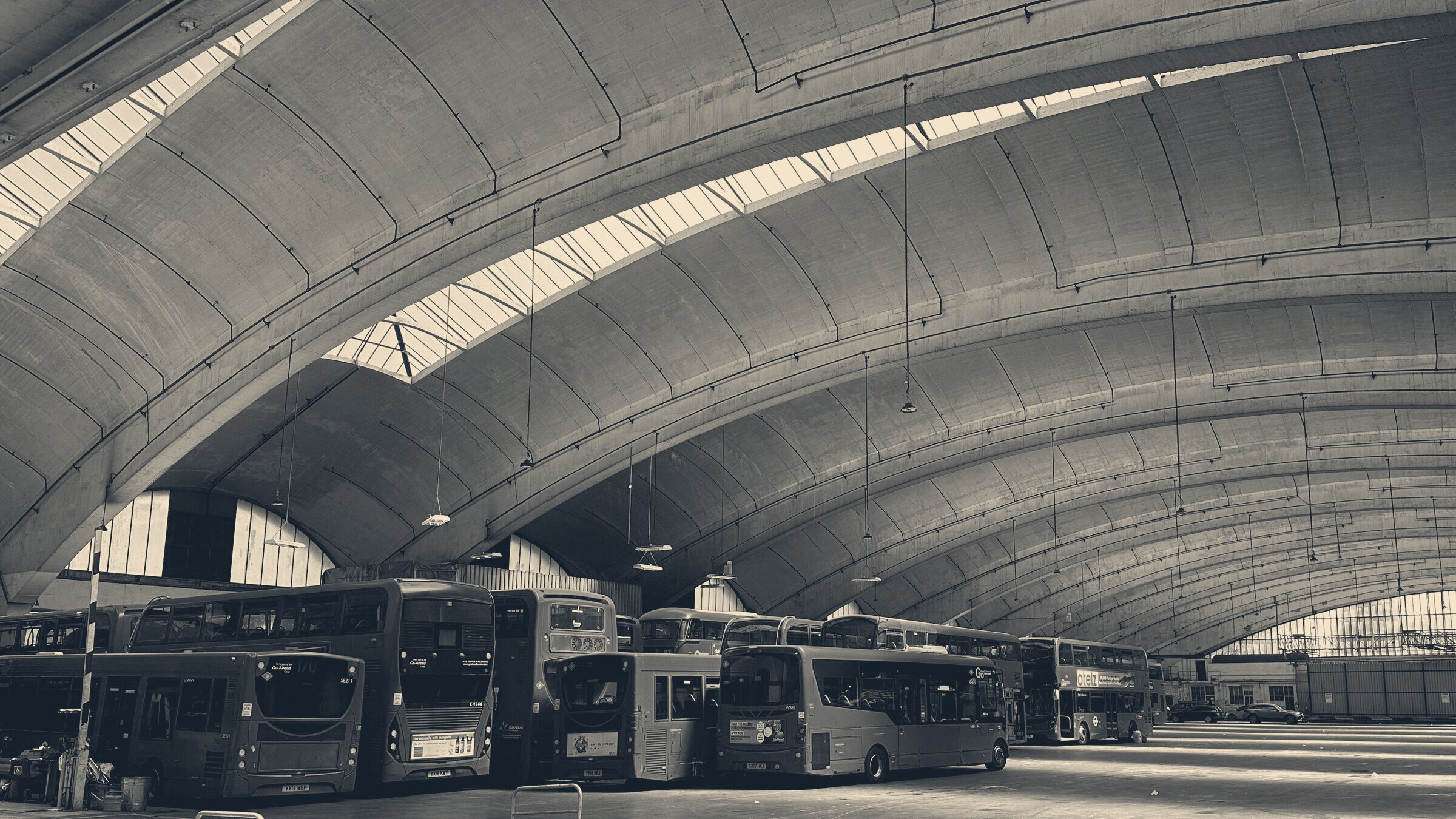 Red London buses parked beneath the soaring concrete cantilever arches of Stockwell Bus Garage.