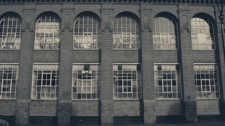 Arched windows of a red-brick Victorian textile factory in Leicester, grilles and blinds hiding the interior.