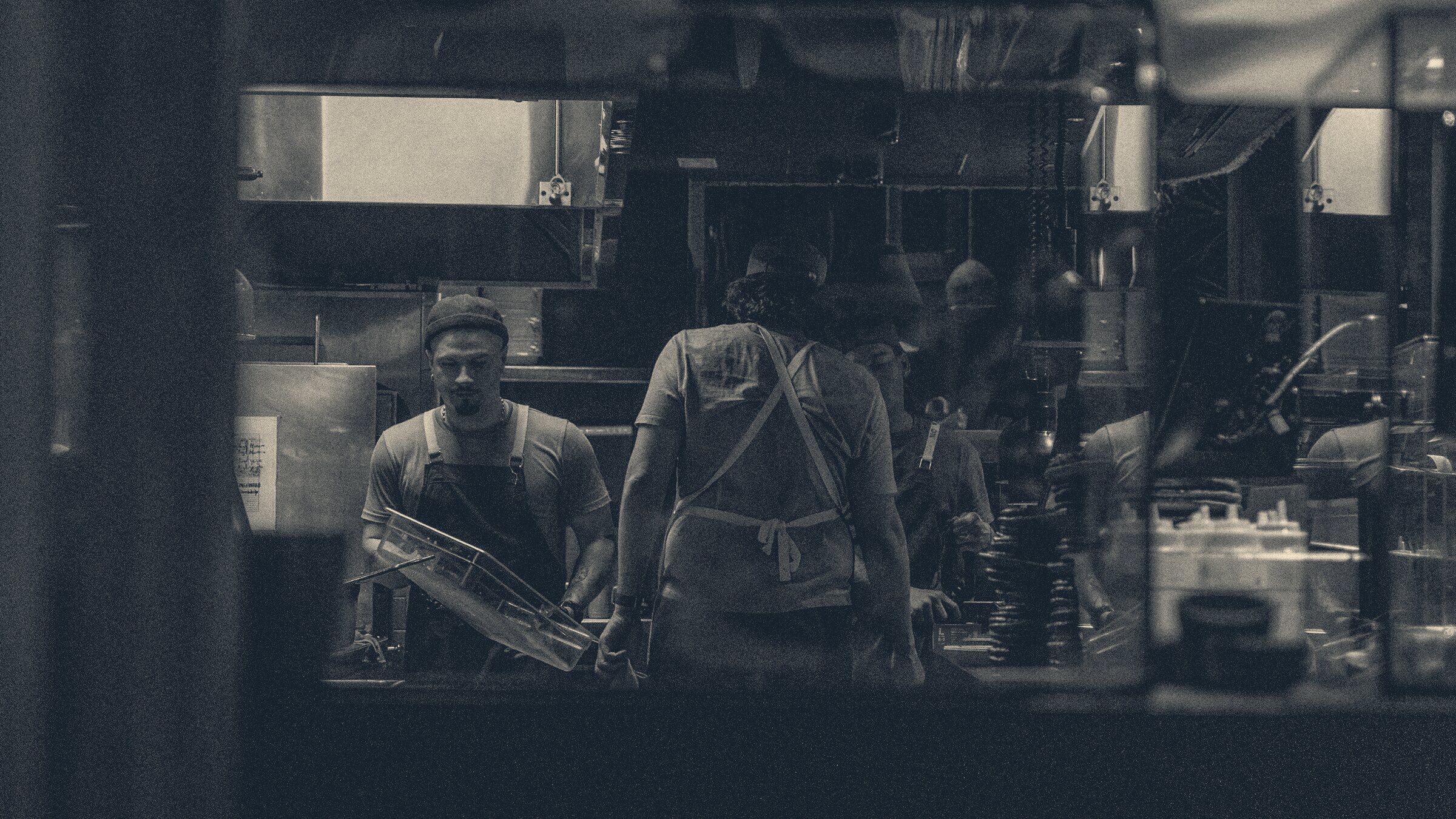 Kitchen workers in aprons seen through a darkened service window during a night shift
