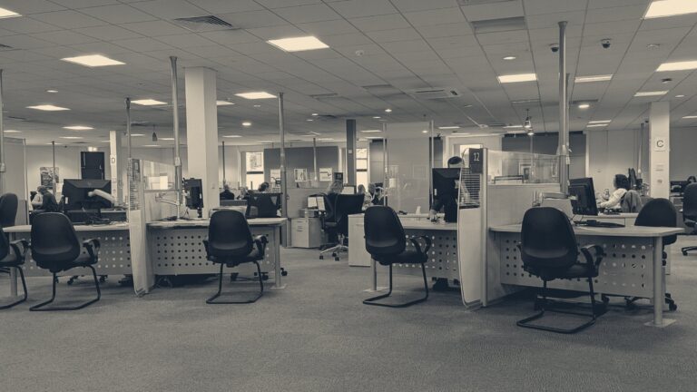 Interior of a Cardiff Jobcentre Plus: numbered desks, computers and seated applicants under fluorescent lights