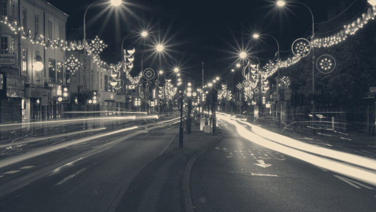 Diwali lights strung across Belgrave Road in Leicester at night, with car light trails along the road