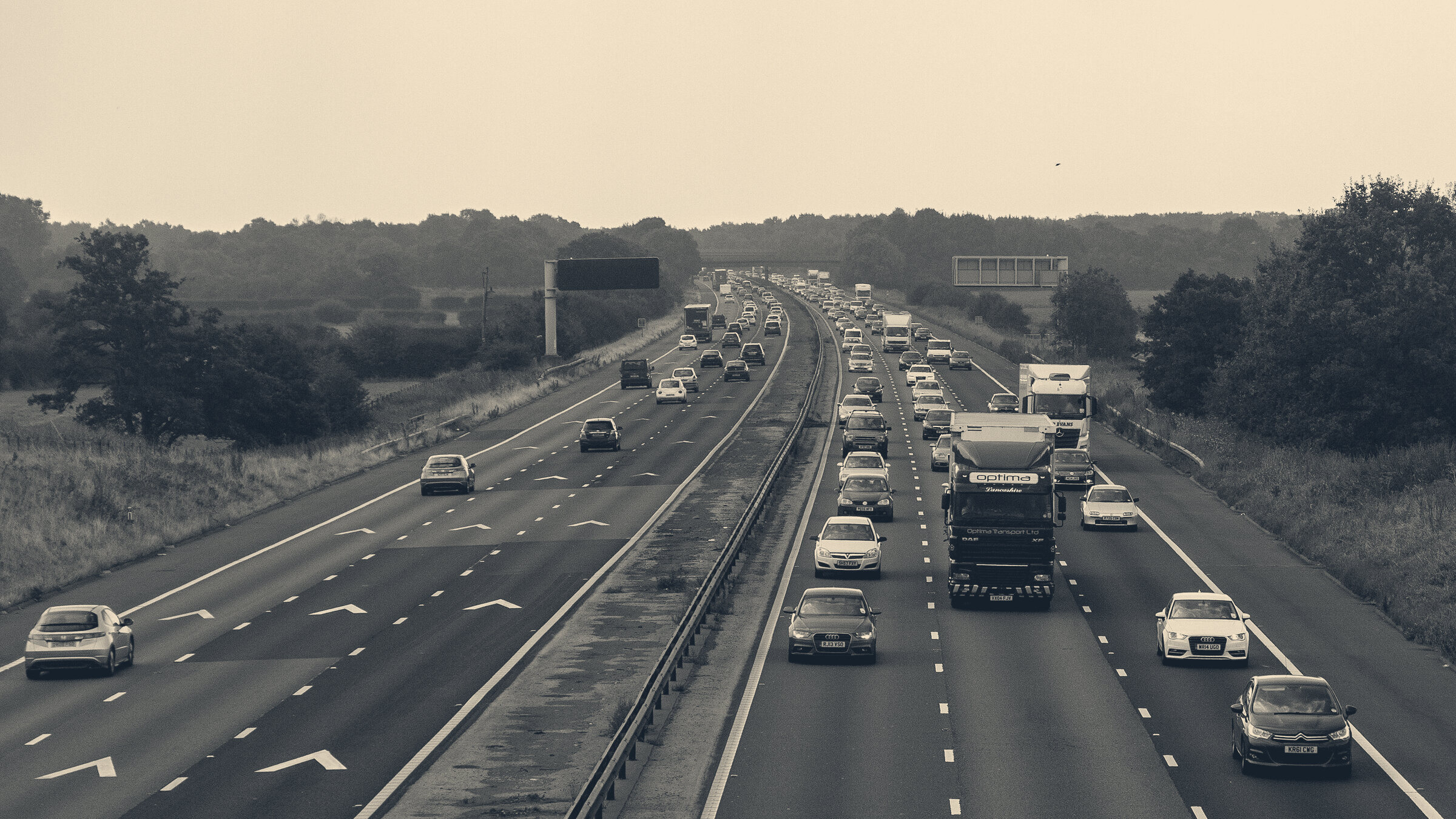 Commercial lorries and commuter traffic flowing along the M6 motorway past safety chevrons under an overcast sky.