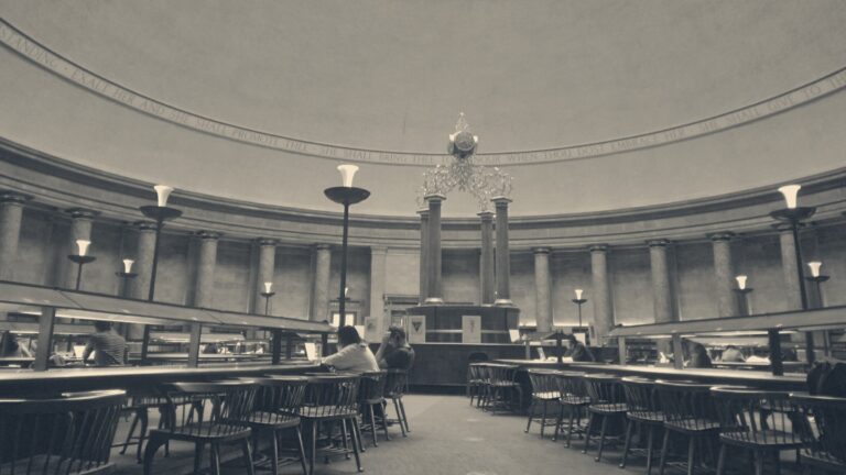 People studying at wooden desks beneath the inscribed rotunda dome of Manchester Central Library.