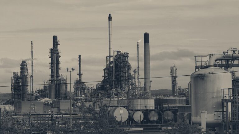Grangemouth oil refinery towers and tanks under a cloudy sky, gas flare burning on a central stack.