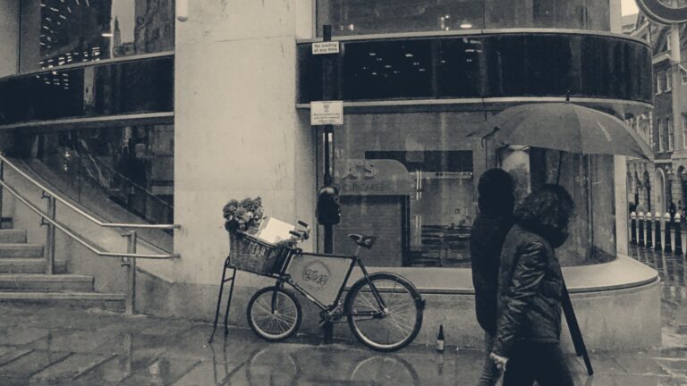 Commuters share an umbrella in heavy rain outside a London Underground station entrance.