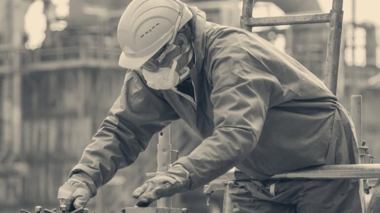 Worker in hard hat, safety goggles, dust respirator and protective gloves inspecting equipment machinery on scaffolding