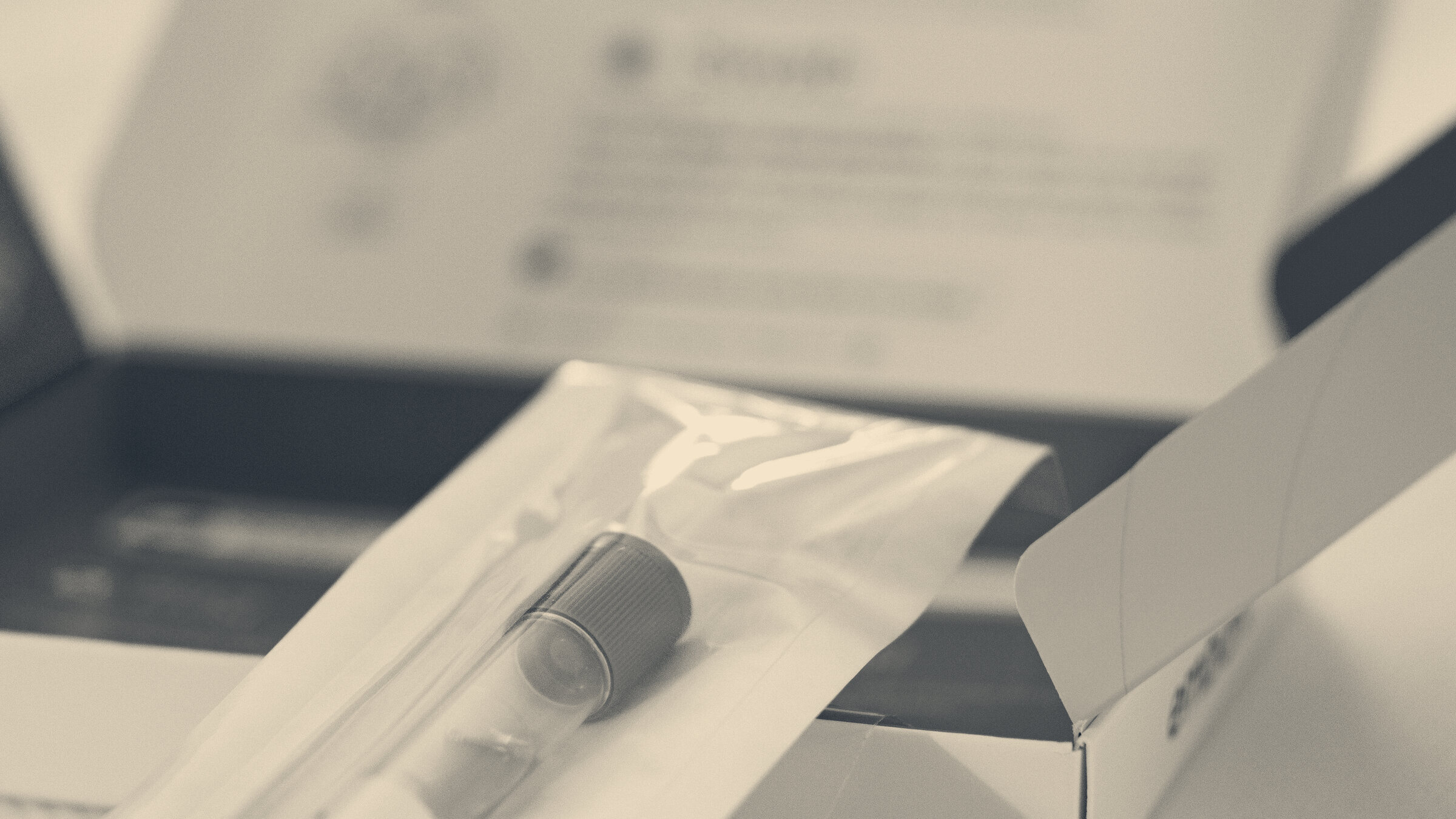 A saliva collection tube with a green cap resting on the packaging of a home DNA test kit, shallow focus